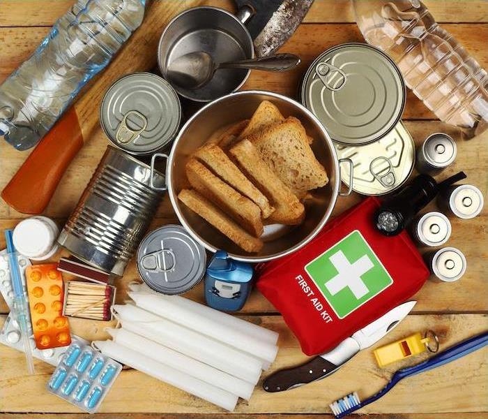 Emergency supplies including food, water, first aid kit, candles, and tools arranged on a wooden surface